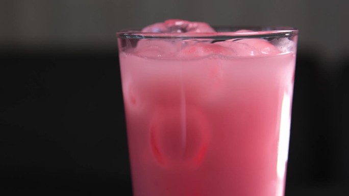 草莓牛奶在一个杯子与条纹纸吸管隔离在黑色背景