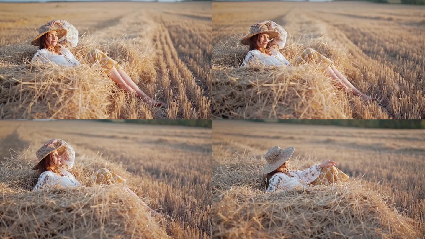 一个漂亮的女人，头戴草帽，身穿绣花上衣，躺在夕阳下乡间的干草上。乡村自然，干草堆，度假，放松和收获的