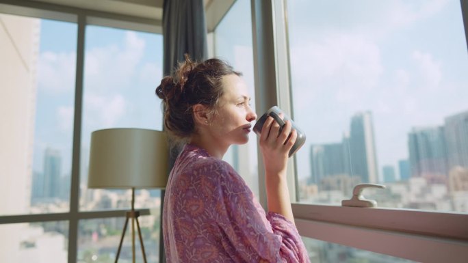 一个女人一边看城市风景，一边喝着早晨的咖啡