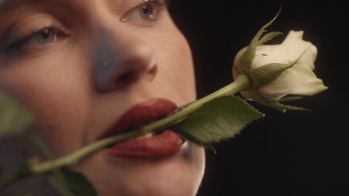性感的女人用红色的口红黑色的背景工作室拍摄的姿势与一个白玫瑰在她的嘴里