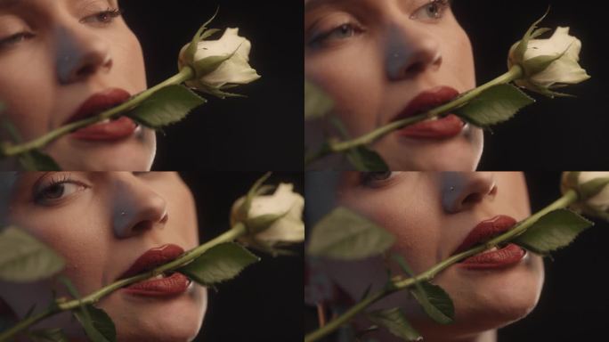 性感的女人用红色的口红黑色的背景工作室拍摄的姿势与一个白玫瑰在她的嘴里