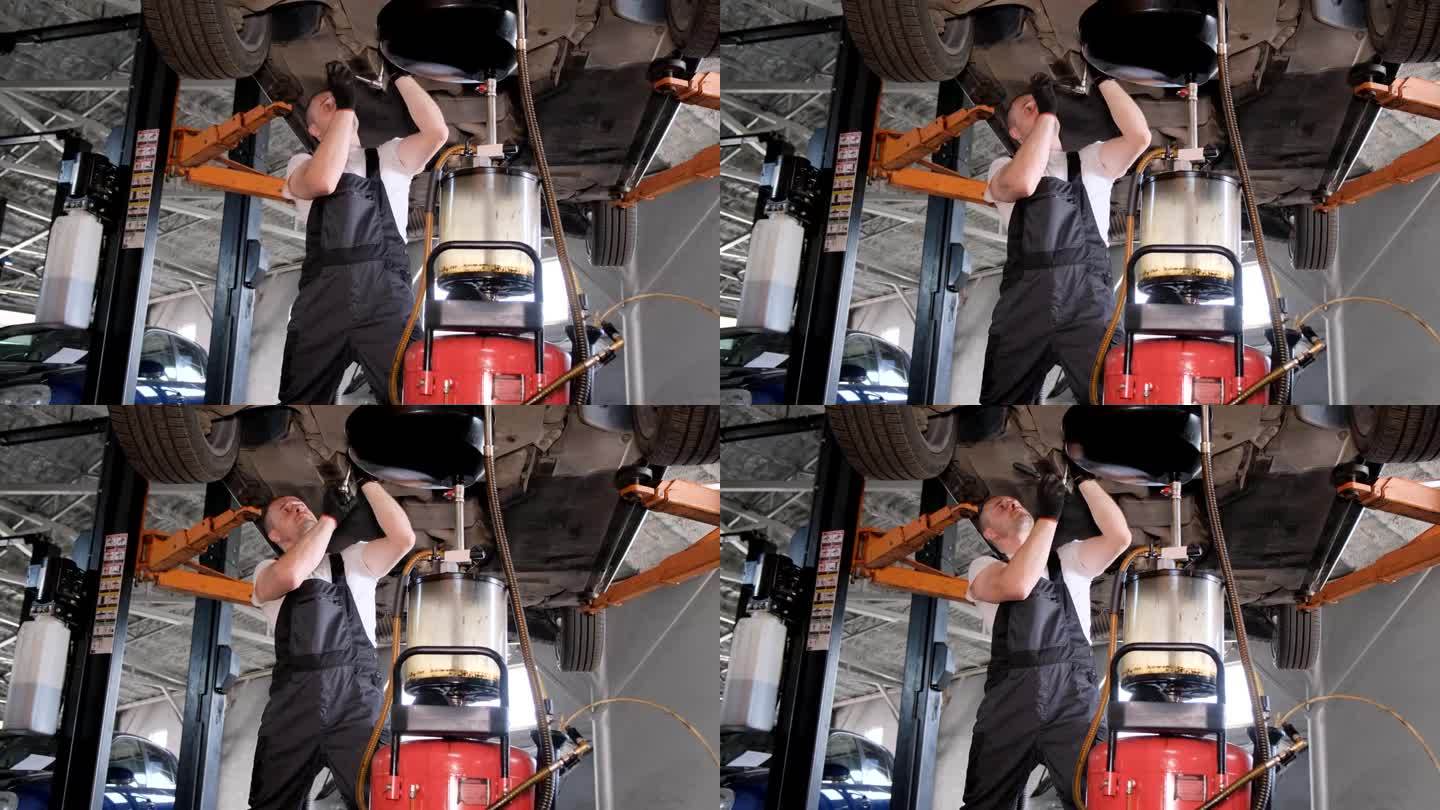 A worker working under a car changes the engine oi