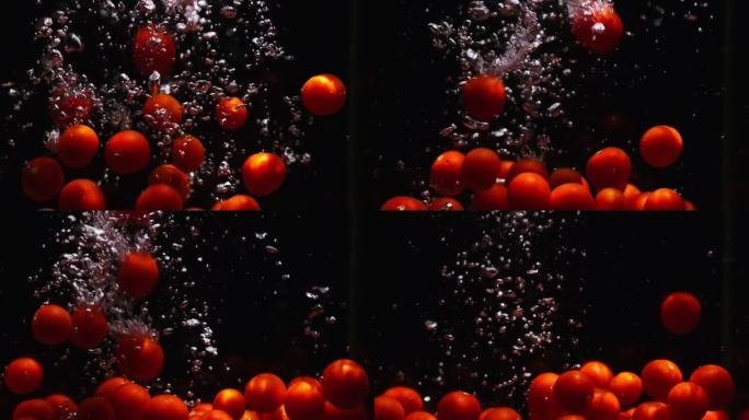 红色成熟的圣女果落在透明的水中，黑色的背景。新鲜的有机蔬菜在鱼缸里飞溅，产生气泡。