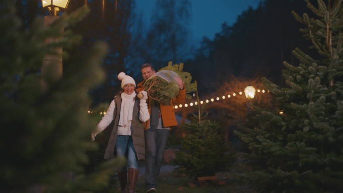 一对夫妇扛着一棵精选的圣诞树穿过圣诞市场