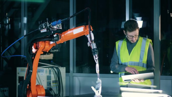 一位研究人员正在使用一台笔记本电脑来控制一个扫描仿生手臂的机器人机构