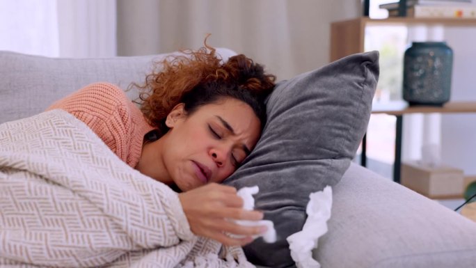 在恢复期，病人、纸巾和躺在客厅沙发上的女人。生病、睡觉和女性在沙发上因流感、鼻窦过敏或感冒而擤鼻涕。