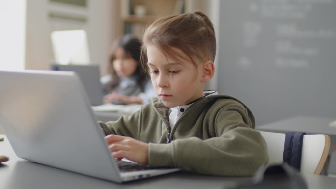 小学生坐在书桌前用笔记本电脑做作业
