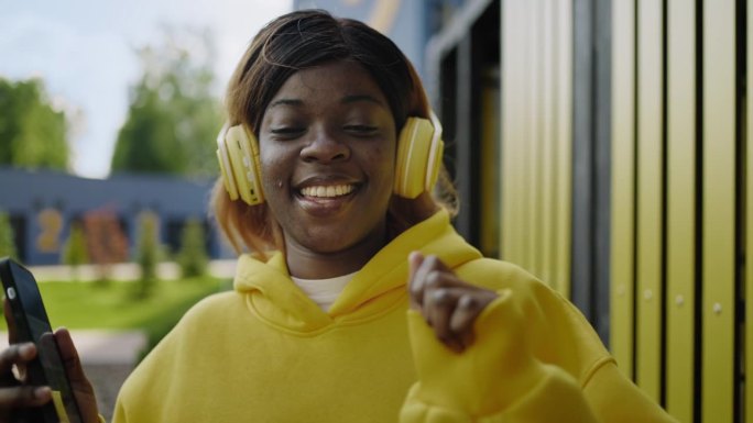 非裔美国女孩走在城市里，唱着歌，戴着耳机听音乐