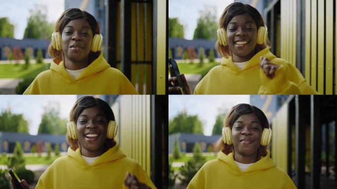 非裔美国女孩走在城市里，唱着歌，戴着耳机听音乐