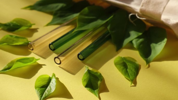 可重复使用的玻璃吸管彩色背景与绿色的叶子在环保袋环保吸管集可重复使用舒适的圆形尖端吸管。零废弃物，无