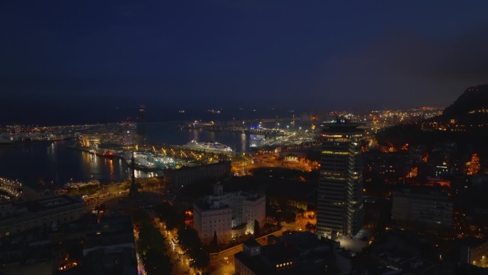 晚上，飞机在市区的建筑物上空飞行。露出水面的船只和灯火通明的港口直到黑夜。西班牙巴塞罗那