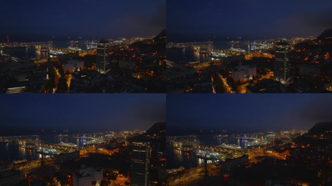 晚上，飞机在市区的建筑物上空飞行。露出水面的船只和灯火通明的港口直到黑夜。西班牙巴塞罗那