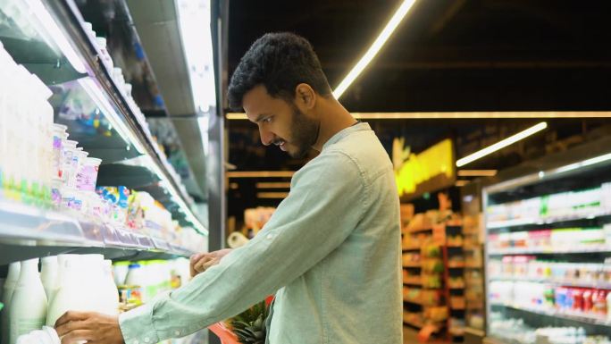 印度帅哥买牛奶的侧视图。一个男人在杂货店买奶制品
