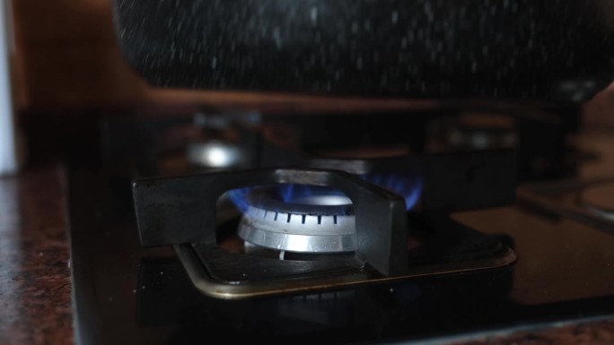 陶瓷黑色煎锅在燃烧的燃气燃烧器上，特写