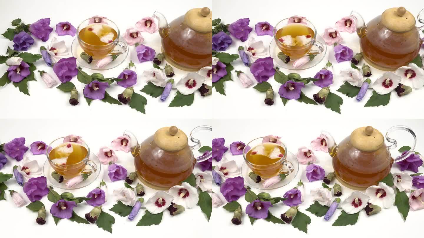 玻璃茶壶和用锦葵花瓣泡茶的杯子，白色的桌子上放着新鲜的锦葵花