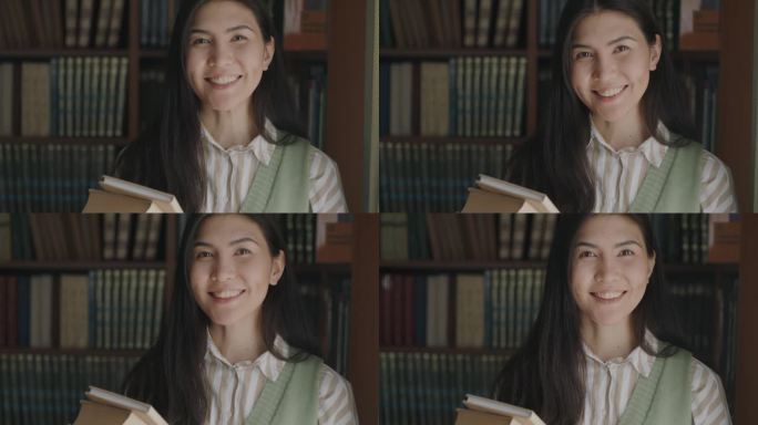 无忧无虑的亚洲女学生站在大学图书馆，拿着书，微笑着看着镜头