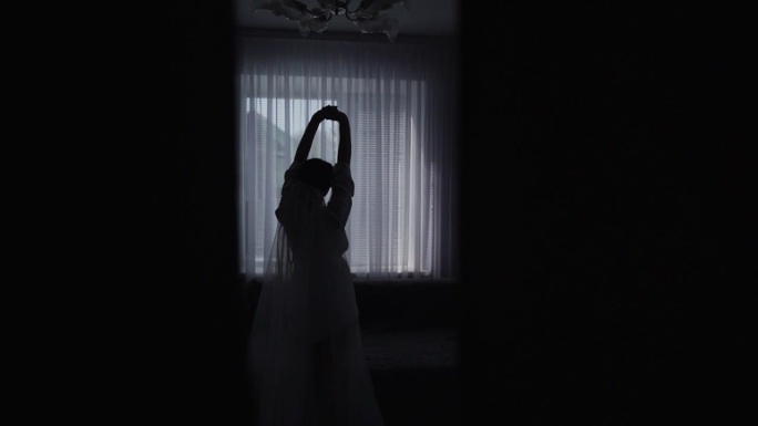 一个美丽性感新娘的剪影透过窗户摆姿势。慢动作