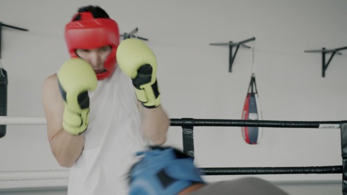 年轻的男子拳击手戴着手套和头盔，在健身房练习拳击，一起做运动