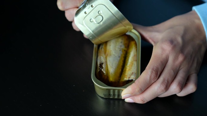 裁剪后的画面聚焦在一个女人打开一罐浸过橄榄油的鲭鱼