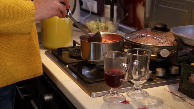 女性用手用长柄勺将煮熟的热葡萄酒倒入玻璃杯中。用平底锅在炉子上煮热红酒。热酒精饮料。