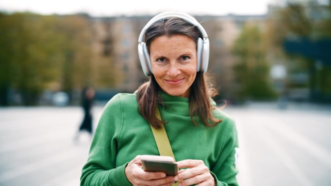 在城市停车场戴着耳机使用智能手机的女子肖像