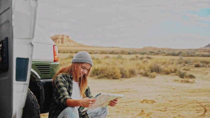 一名妇女在沙漠某处的一辆露营车前看地图