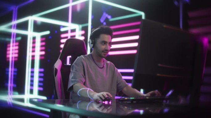 一个年轻人在一个充满未来感的霓虹灯房间里玩动作电子游戏。帅哥戴上耳机和在线流媒体观众交谈。流媒体和游