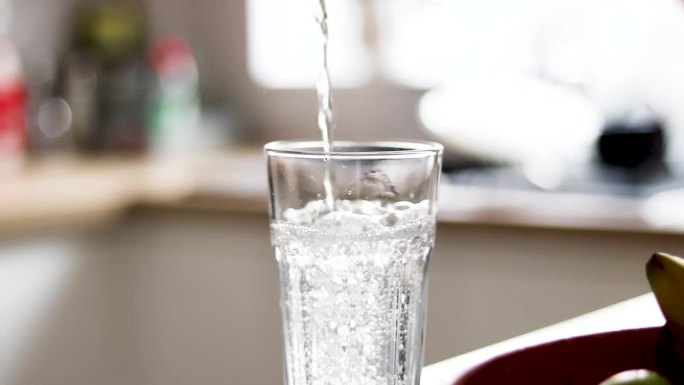 靠近一杯水，柔焦。从厨房台面的瓶子里倒出纯净的新鲜干净的饮用水到玻璃杯里