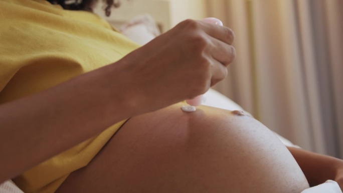 一位非洲孕妇在腹部涂抹面霜。