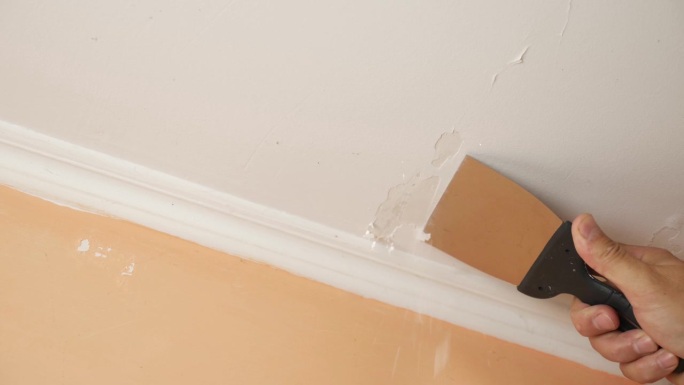 用抹刀把天花板上残留的旧油漆刮掉。施工工程。