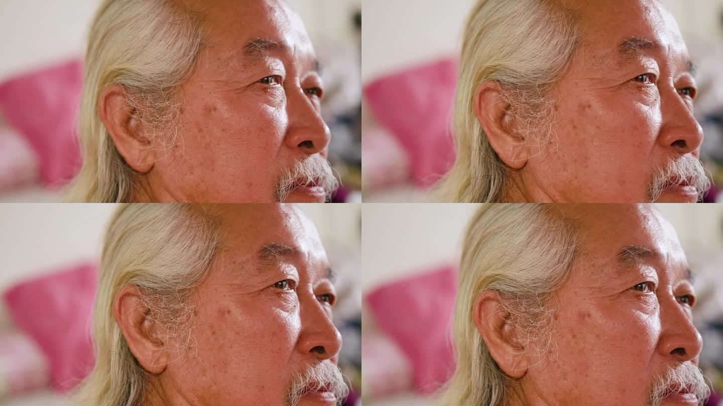 一位亚洲老人看电视，脸上带着严肃的表情。