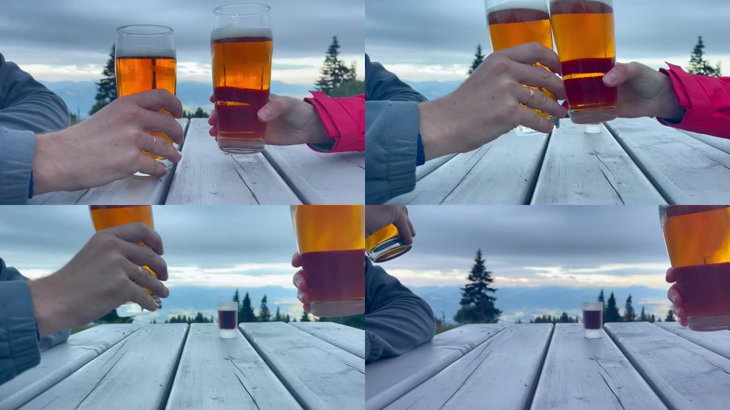 近距离的4K镜头，两名徒步旅行者坐在山间小屋露台上的木桌旁，用两个大啤酒杯碰杯。软饮料，酒精，饮料和
