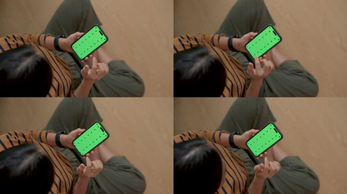 一个女人拿着智能手机，坐在家里的地板上滚动着绿屏模型。