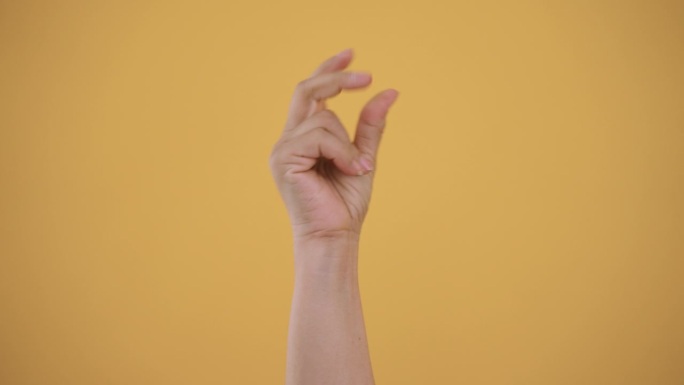 女人的手在黄色背景上打着响指。