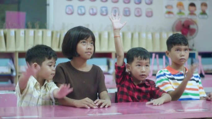 一群学校的亚洲孩子坐在教室里，举起手臂回答老师的问题。回归学校和教育理念。慢镜头。