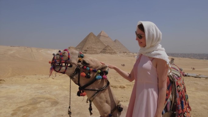 在埃及，一名年轻女子站在一头骆驼旁边。