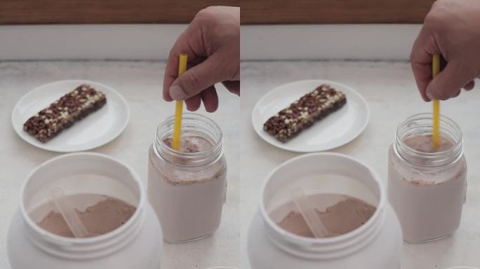 男手用吸管将乳清蛋白粉与牛奶混合在玻璃罐中，制作蛋白饮料冰沙的过程，运动营养，垂直视频