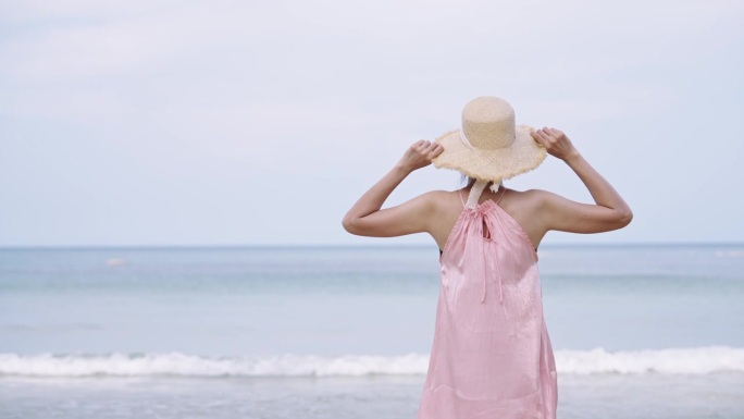慢动作女人走向海滩，拿起她的遮阳帽，看着风景