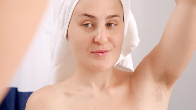 穿着浴巾的快乐微笑的女人看着她腋下长出的头发。美丽女性的概念，自然美，女性气质和体毛