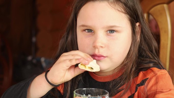 专注，热情，肥胖的黑发小女孩嚼着沙瓦玛或三明治，喝着茶。暴饮暴食