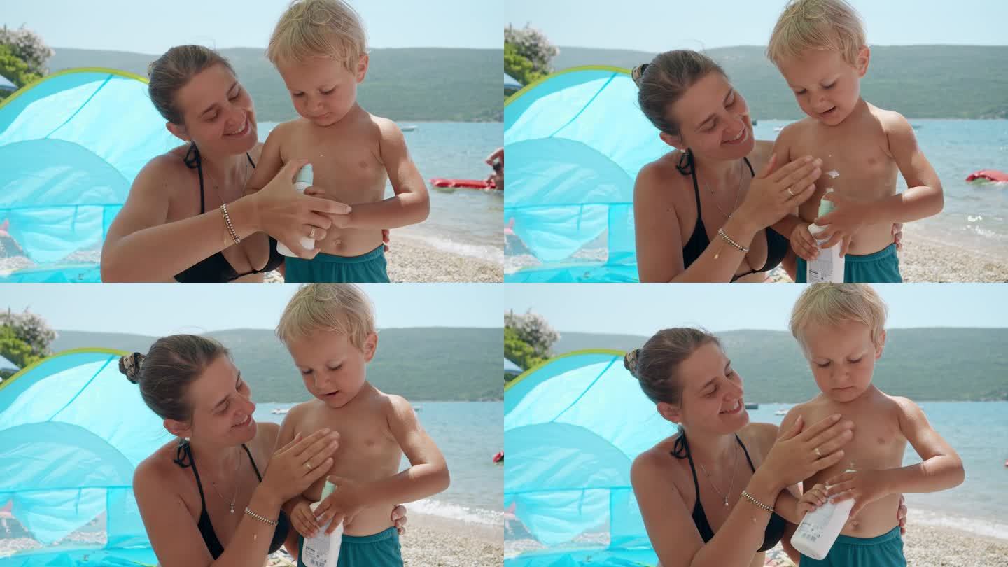 在阳光明媚的海滩上，一位可爱的年轻母亲孜孜不倦地给她的儿子涂抹防晒喷雾。医疗保健和家庭度假的概念。