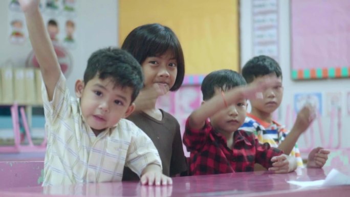 一群学校的亚洲孩子坐在教室里，举起手臂回答老师的问题。回归学校和教育理念。慢镜头。