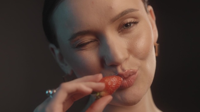 性感的女人用红色的口红黑色的背景工作室拍摄的姿势亲吻草莓