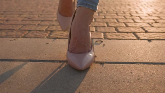 穿着高跟鞋的苗条女性漫步在城市公园的夕阳下。