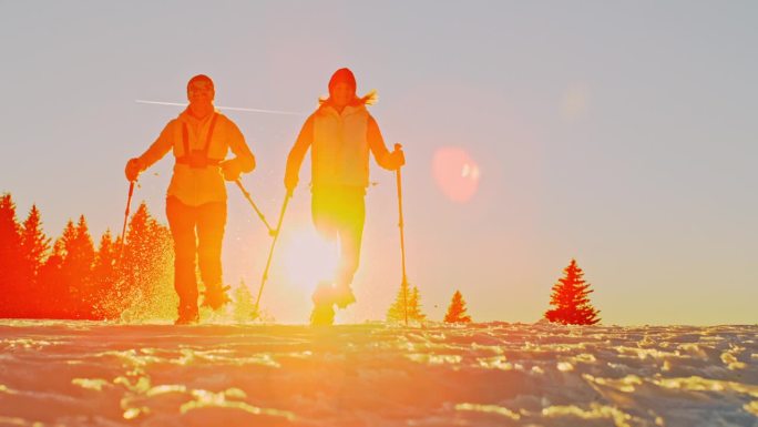 日落时分，两个徒步旅行者穿着雪鞋在雪地上奔跑