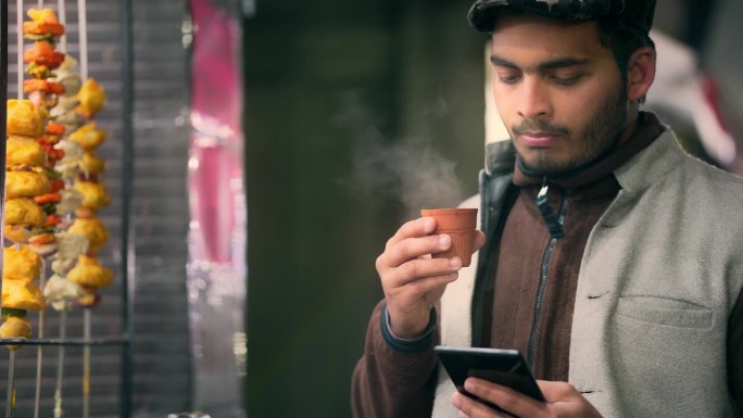 一名男子一边用智能手机一边用库拉德/陶杯喝茶。