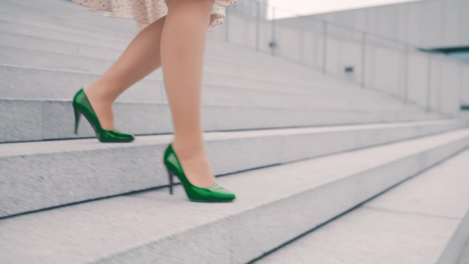 一个不知名的女人穿着裙子和绿色高跟鞋走下一座现代建筑前的楼梯