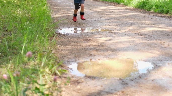 穿着橡胶靴的孩子的脚在水坑里跳跃。穿着惠灵顿长靴的孩子们在泥泞中戏水。小男孩在泥里玩耍。户外玩耍的孩