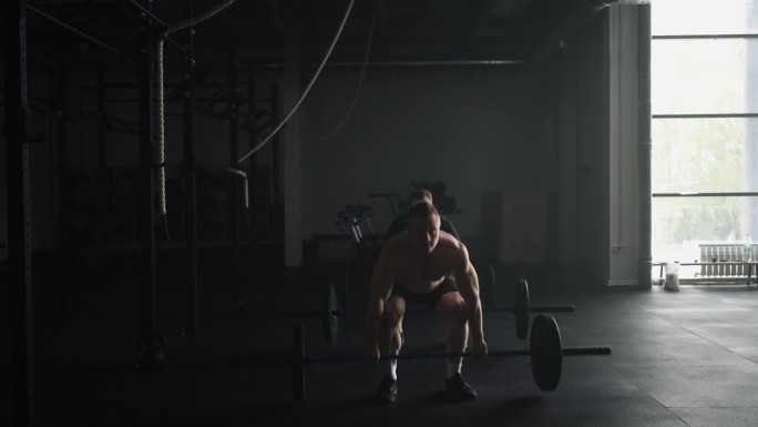 两个举重运动员在健身俱乐部举杠铃，黑暗中肌肉发达的男性剪影