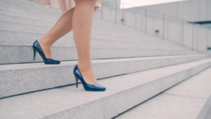 一个不知名的女人穿着裙子和蓝色细高跟鞋走下城市的楼梯